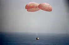 Un vaisseau spatial descend au-dessus de l'océan avec des parachutes.