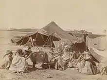 Photographie montrant une famille installée devant une tente, dans le désert.