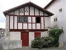 Vue d'une maison à un étage, chaulée avec pans de bois peints en rouge.