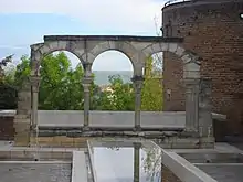 Arcs outrepassés en pierre ; à droite, une tour de l'enceinte médiévale, d'où partait aussi le mur des chanoines et au premier plan, un bassin de construction récente.