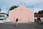 Photographie d’un homme jouant à la pala sur le mur d’un fronton rose.