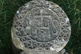 Photographie d’une stèle discoïdale en pierre, sur fond d’herbe.