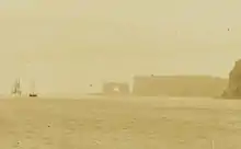 Photographie en sépia de l'arche des Kerguelen avant qu'elle ne s'effondre, avec deux navires à voile au mouillage à proximité