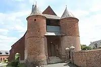 La façade fortifiée est flanquée de deux tours percées de meurtrières et ornées de motifs en briques vernissées.