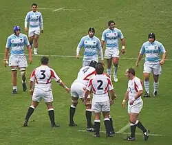 Cinq joueurs argentins se dirigent pour former l'alignement de la touche alors que les joueurs anglais sont prêts, alignés perpendiculairement à la touche pour soutenir leur sauteur.