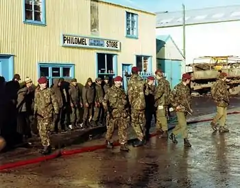 Photo d'un groupe d'hommes alignés contre le mur d'un bâtiment, entourés d'hommes armés vêtus de treillis