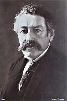 Portrait en noir et blanc d'un homme moustachu aux cheveux grisonnants, portant cravate et costume trois pièces
