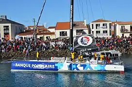 Le bateau avance dans le chenal des Sables-d'Olonne. Debout à l'avant, Le Cléac'h salue la foule.