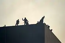 Silhouettes de personnes sur un toit lançant des projectiles.