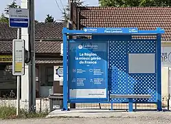 Un abribus de couleur bleue. À gauche de l'image se trouve un poteau d'arrêt de bus où il est écrit "Saint-Cyr-sur-Menthon - Place Lamberet".