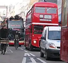 Photographie montant, dans une rue de Londres, une file de bus à impériale, doublés par des vélos.