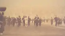 Image jaunie où l'on voit un coureur en blanc entouré de nombreux hommes en costumes noirs.