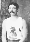Un homme à moustache en tenue de sport blanche.