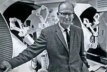 Photographie en noir et blanc d'un homme en veston portant une cravate noire et des lunettes