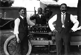 Photo de trois hommes prenant la pose autour d'une voiture qu'ils travaillent.