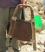 La main d'un homme portant un arceau formé de la tige d'une plante encadrant un sac en cuir, et raccordé par le côté droit à la partie inférieure d'une bouteille en plastique vert.