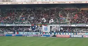 vue d'une tribune derrière un but, les supporters brandissant des drapeaux.