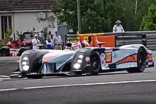 Photographie d'une voiture de sport-prototype bleu, noir et orange, vue de trois-quarts, sur une piste.