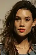 Portait d'une jeune femme aux cheveux bruns et longs, portant un rouge à lèvres rouge vif et regardant le photographe.