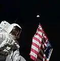 Harrison Schmitt pose avec le drapeau américain et la Terre en arrière-plan au cours de la première EVA d'Apollo 17. Eugene Cernan est visible, par réflexion dans la visière du casque de Schmitt.