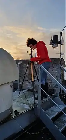 Photographie en couleurs d'une astrophysicienne penchée sur un instrument d'observation.