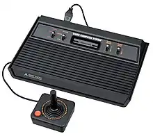 Photographie d'une console de jeux vidéo noire sur laquelle est reliée une manette.