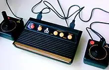 Boite noire avec deux manettes de jeux noires, comportant quelques pointes de marron et des boutons jaunes.