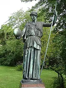 Statue de bronze d'une femme tenant un casque et une lance, dans un jardin