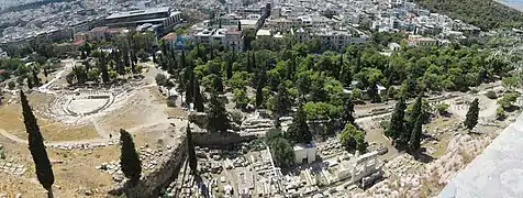 La stoa d'Eumène relie le théâtre de Dionysos, à gauche, à l'odéon d'Hérode Atticus, à droite hors de l'image. Vue prise du rempart sud de l'Acropole.