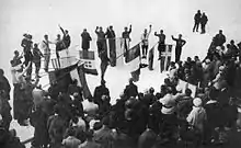 Une photographie en noir et blanc représentant un groupe de porteurs de drapeaux formant un cercle