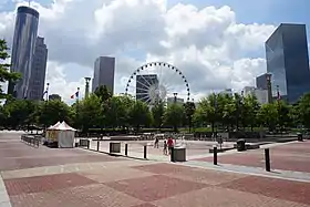 Des fontaines d'eau sont d'une place recouverte de petites briques orangées et rouge du parc du Centenaire. Au second plan, on aperçoit une grande roue.