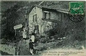 Carte postale ancienne avec un homme et deux femmes vêtues de tabliers devant café-restaurant.