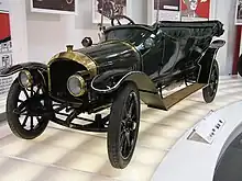 Une voiture ancienne dans un musée, toit découvert, haute calandre, grands phares ronds.