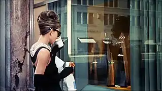 Audrey Hepburn, en tenu de soirée, buvant un café à emporter et avec un croissant à la main, devant la vitrine du joailler Tiffany à New York