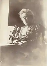 Photographie en tons sépias d'une femme assise à côté d'un microscope, tenant une lame.