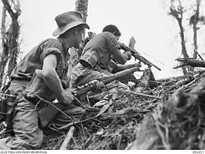 Photographie en noir et blanc de deux soldats australiens se cachant derrière un remblai. L'un pointe son fusil vers le haut.