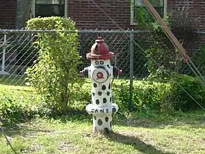 une bouche d'incendie repeinte en blanc à pois noirs avec un visage, ressemble à un clown triste