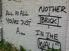 Mur en brique blanc sur lequel est taguée, en noir, la phrase « All in all you're just a… nother brick in the wall ».