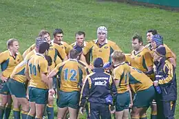 Joueurs de rugby regroupés en cercle, certains s'abreuvant.