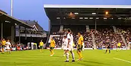 vue d'un match de football entre une équipe évoluant en blanc et une en jaune dans un stade aux tribunes à moitié pleine
