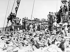 Photo en noir et blanc d'une cinquantaine d'hommes rassemblés sur le pont d'un navire. Ceux qui sont au premier plan sont en train de se bronzer. Ceux qui sont à l'arrière-plan tournent le dos à l'objectif.