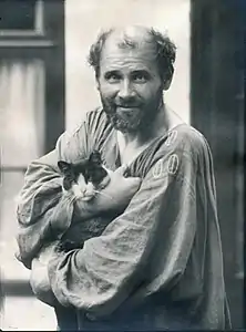 Photo noir et blanc en plan taille d'un homme dégarni barbu, en blouse brodée et portant un chat dans ses bras