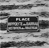 Plaque noire qui indique la place « Hippolyte de Barrau » en écriture blanche.