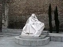 Statue de marbre blanc, posée dans une cour, représentant une religieuse assise.