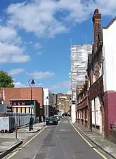 Une longue rue étroite et déserte. Du côté droit de la rue, une longue rangée de chalets traditionnels anglais faits de briques rouges. Du côté gauche, des bâtiments modernes.