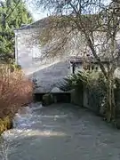 Vue d'un bâtiment établi au-dessus d'un cours d'eau. Vestiges d'une roue à aubes visible sous le bâtiment.