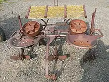 Ancien plantoir à pommes de terre, avec deux sièges-baquets en métal, table inclinée devant, et outils de calibrage derrière