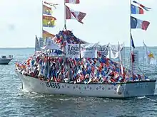 Vue du bateau de pêche The Breau's II au port de Caraquet, durant la bénédiction des bateaux. Il est décoré du drapeau du Nouveau-Brunswick, du drapeau du Canada, du drapeau de l'Acadie et de guirlandes de fanions bleus, blancs et rouges.