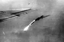 Photographie en noir et blanc d'un appareil en flammes plongeant vers le sol.