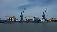 Photographie d’un cargo porte-container bleu, à quai dans un port.